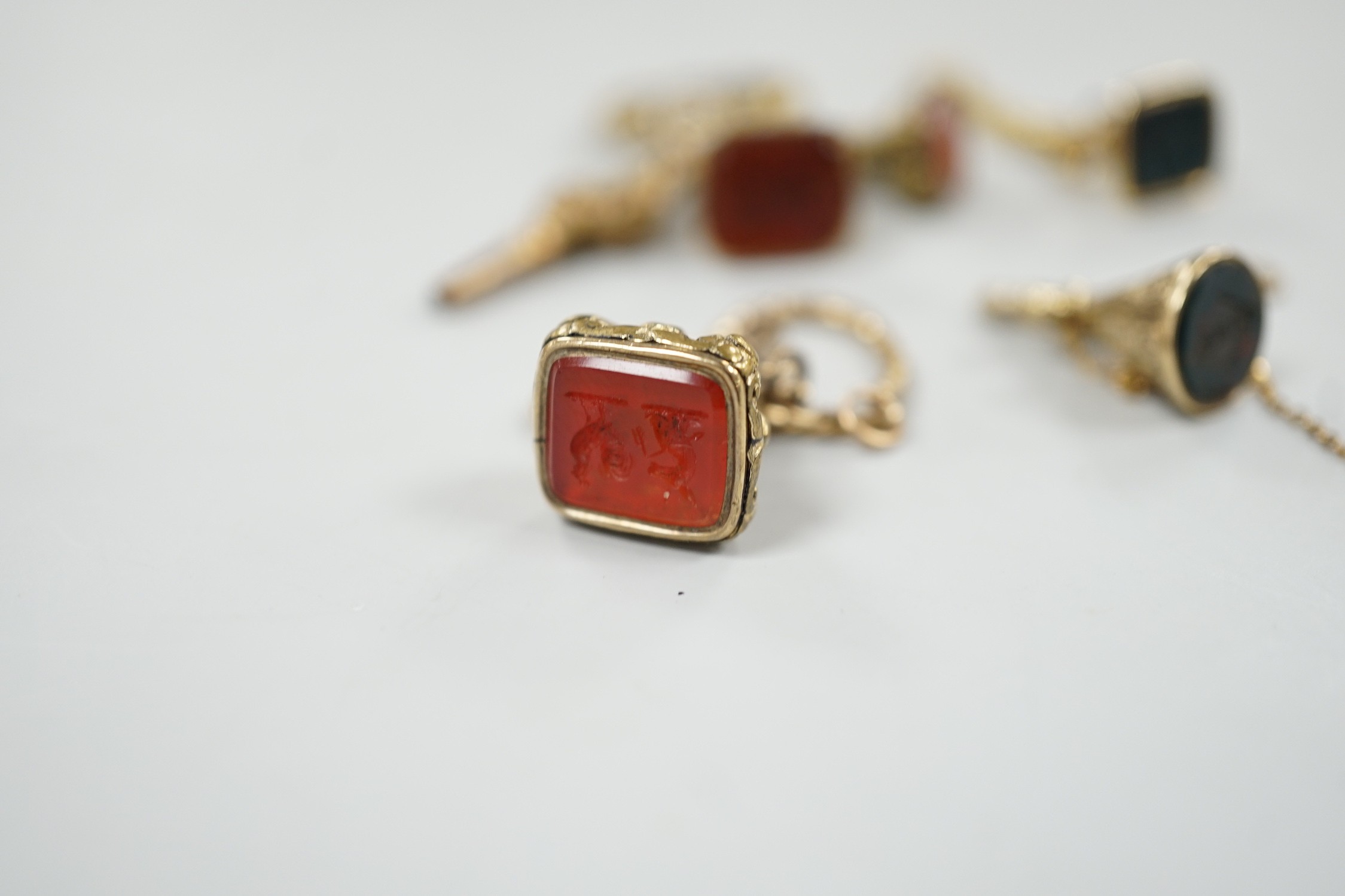Two 19th century yellow metal overlaid and bloodstone set watch key fobs, one of funnel form, 21mm, a similar gold plated and carnelian set watch key fob, two other fob seals and a watch key on chain.